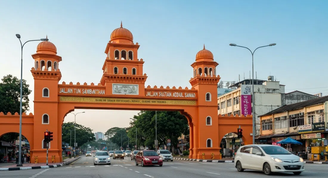 la Puerta Torana de color naranja brillante en el cruce de Jalan Tun Sambanthan y Jalan Sultan Abdul Samad, enmarcada de frente con luz de la tarde y tráfico del Pequeño India pasando debajo